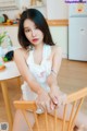 A woman sitting on a wooden chair in a kitchen.