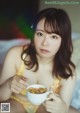 A woman sitting on a bed holding a bowl of cereal.