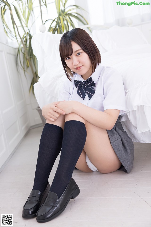 A woman in a school uniform sitting on the floor.