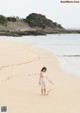 A woman in a white dress walking on a beach.