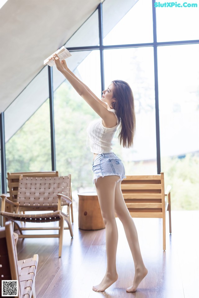 A woman standing in front of a large window holding a book.