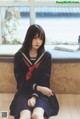 A woman in a school uniform sitting on the floor.