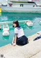 A woman in a school uniform sitting on the edge of a pier.